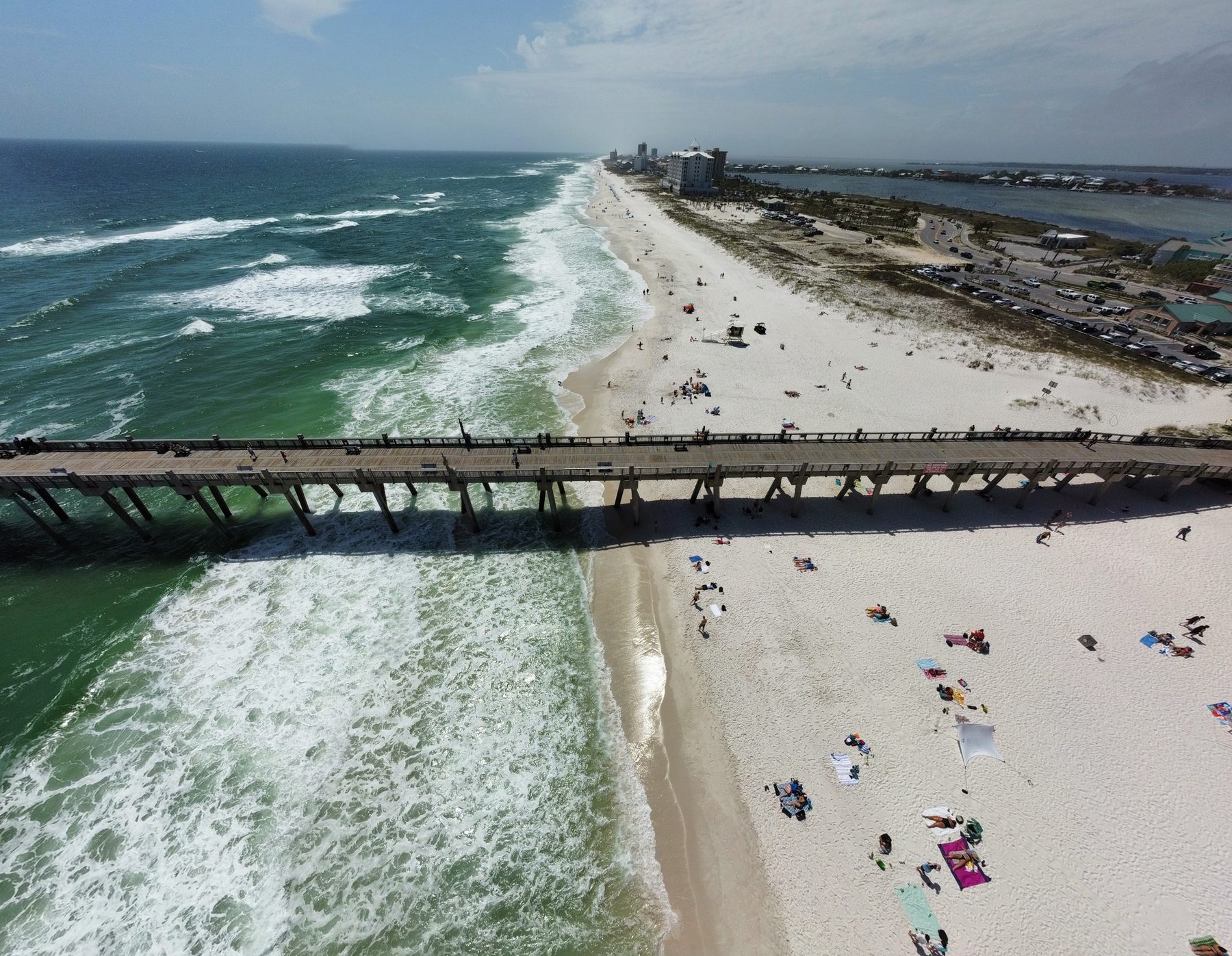 Aerial drone view of the Pensacola Beach Gulf Pier stretching over emerald surf and white-sand beach