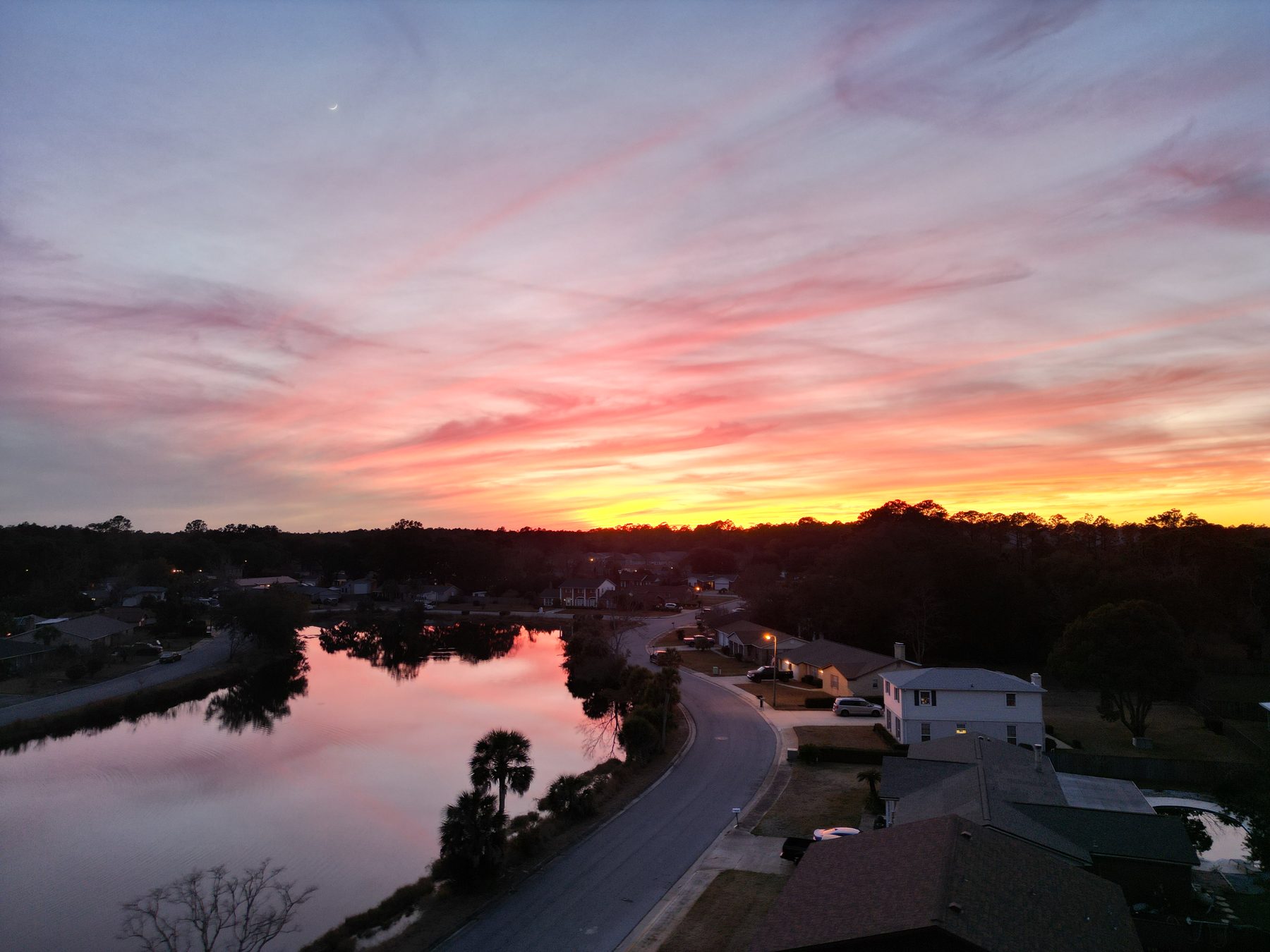 Vivid pink and orange sunset over a Gulf Coast waterway and neighborhood, captured by drone