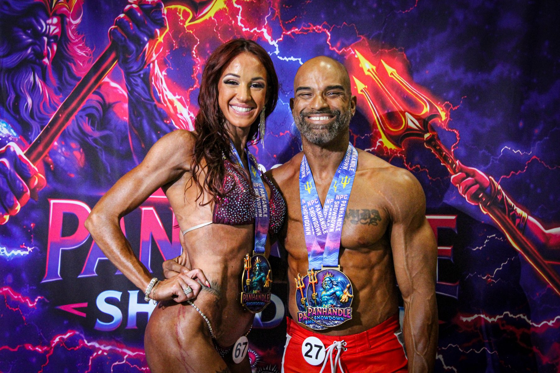 Two physique athletes celebrating with medals in front of the Panhandle Showdown backdrop