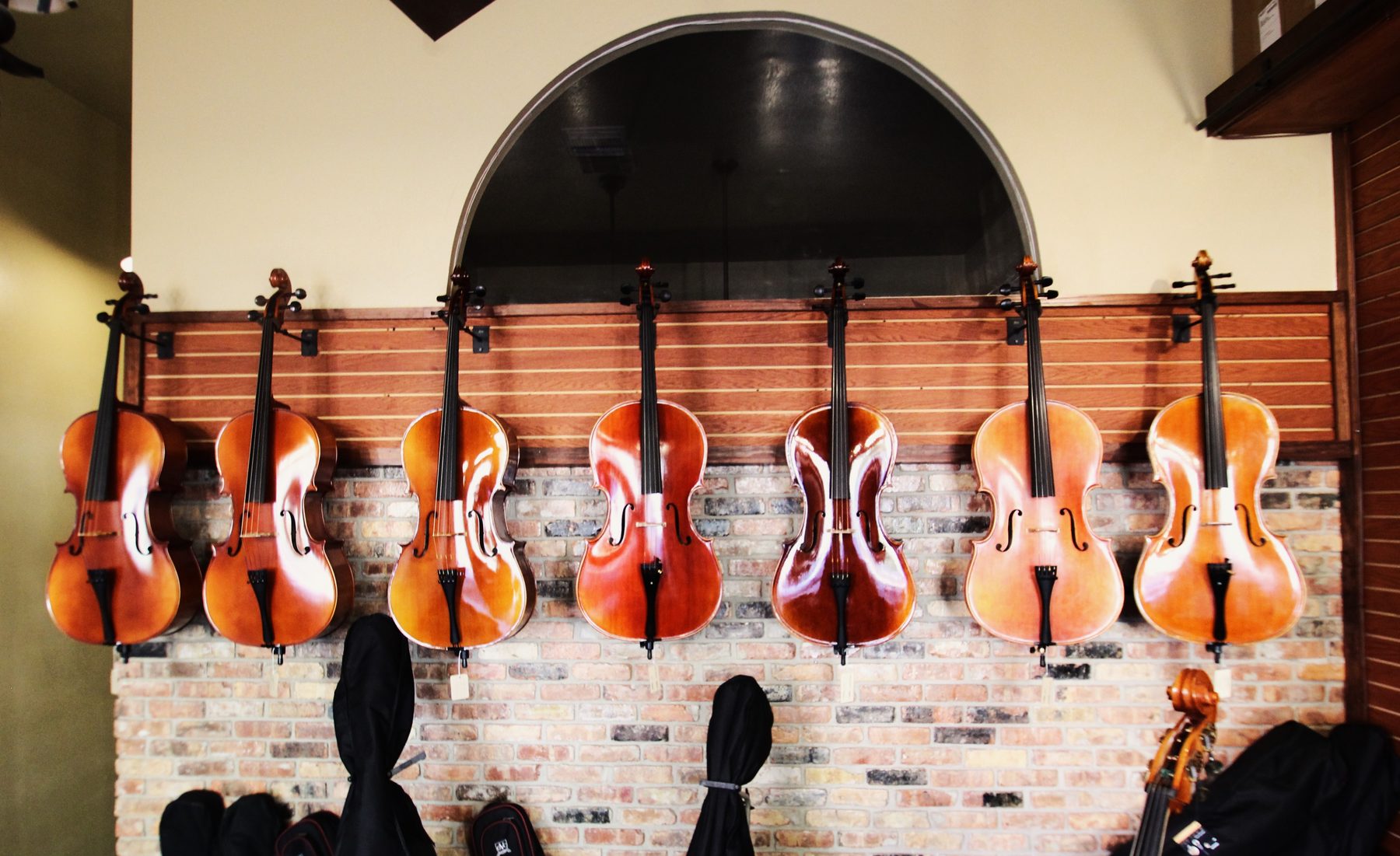 Wall of violins and cellos hanging against exposed brick in a Pensacola string instrument shop
