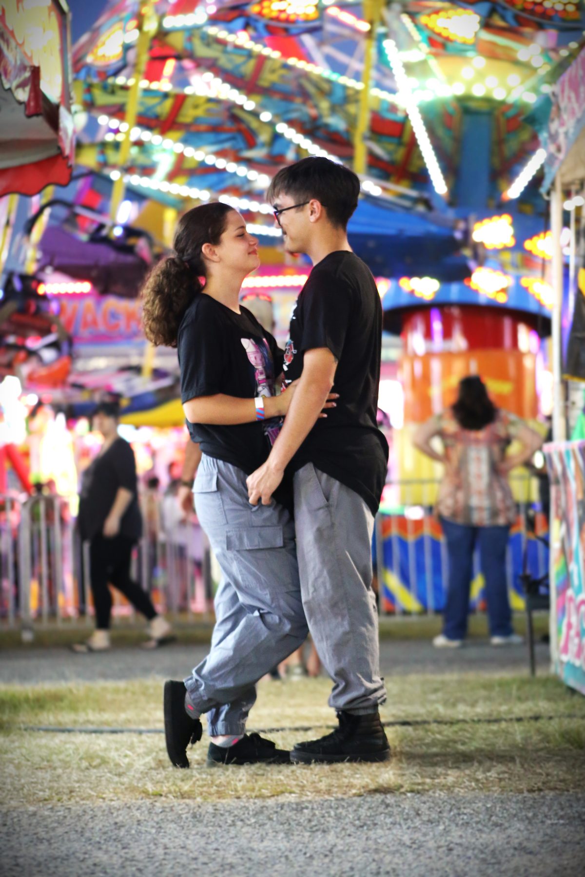 Young couple facing each other in front of carnival ride lights at the fair