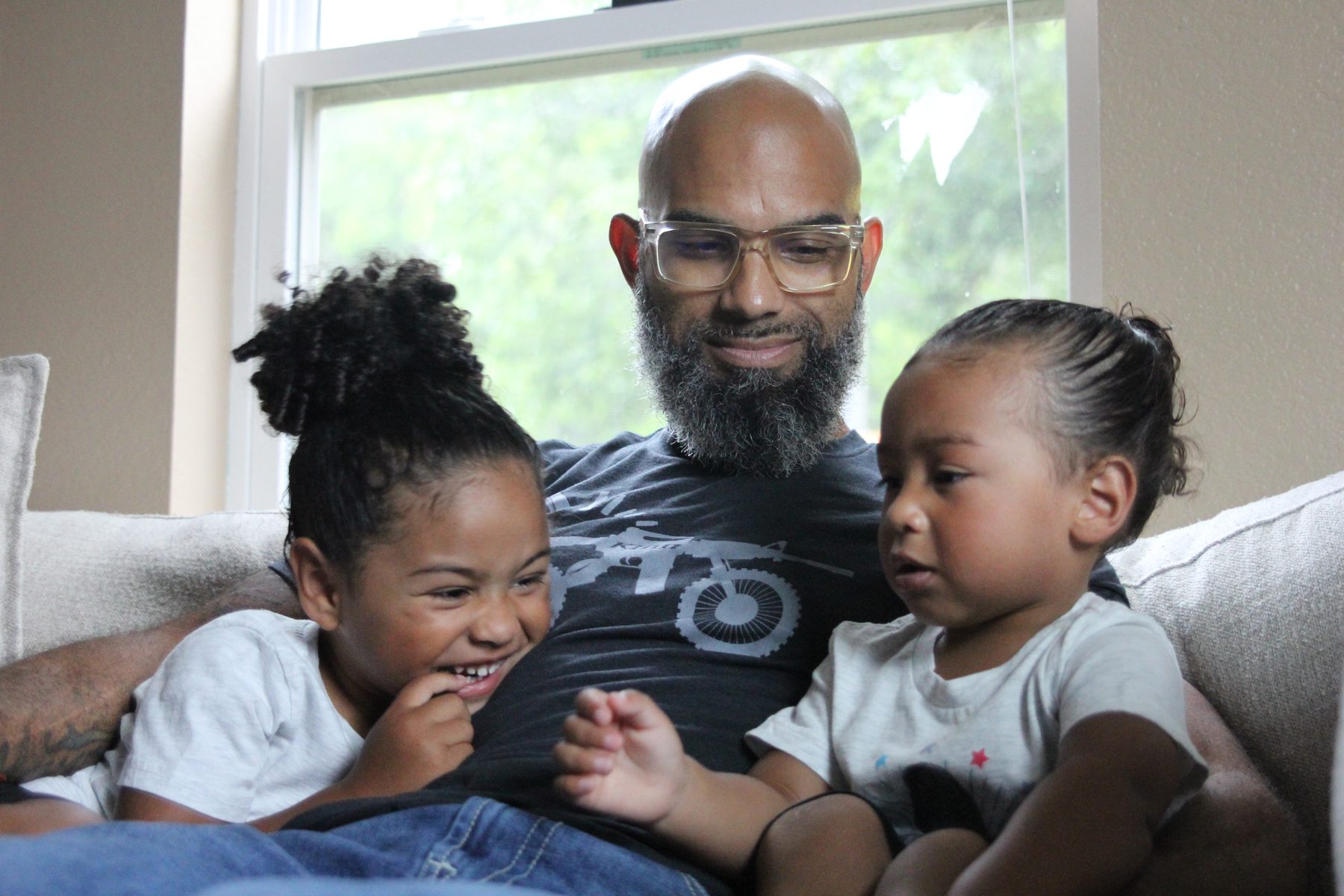Father laughing with his two young daughters on the couch at home