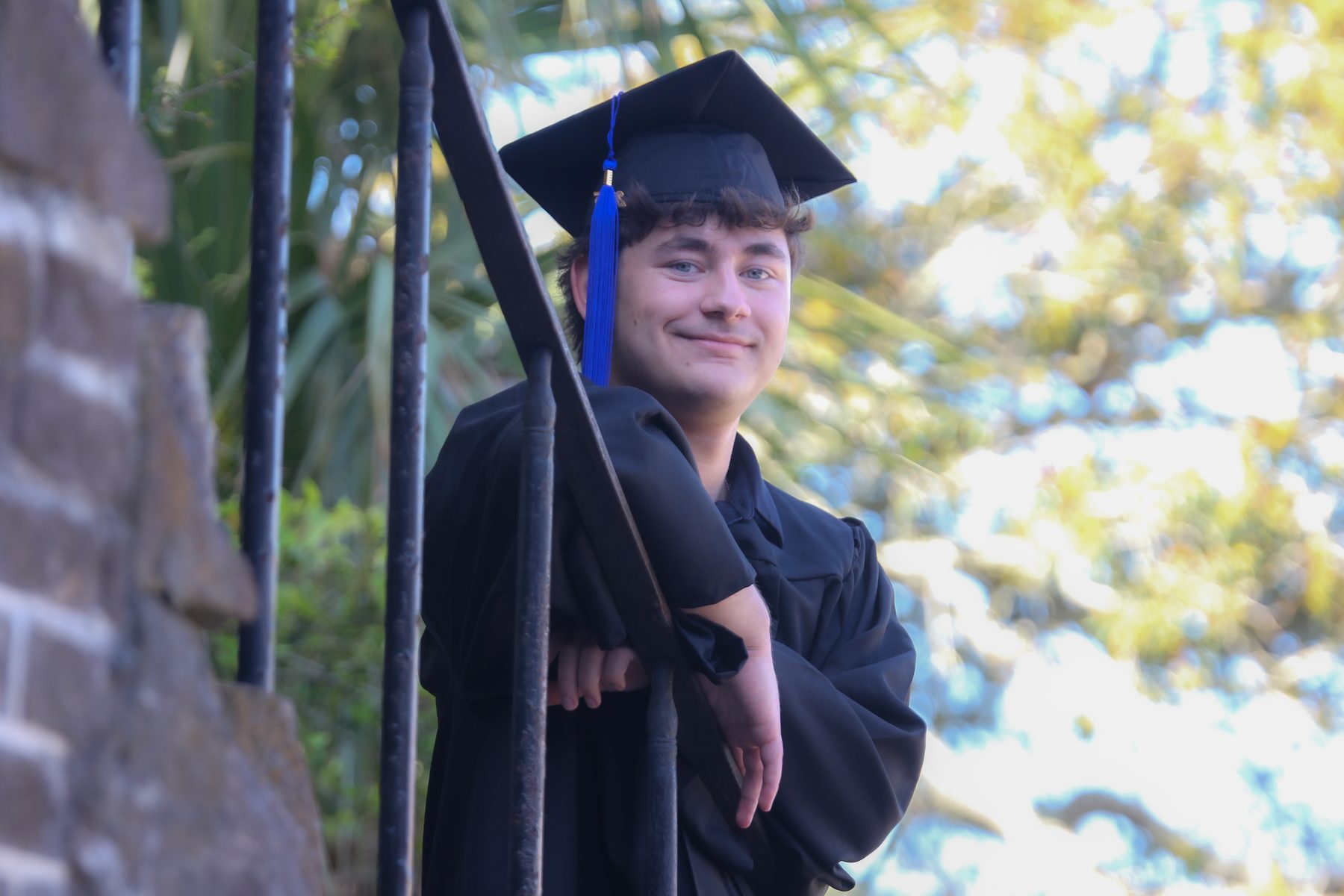 Graduate in cap and gown leaning on historic iron railings