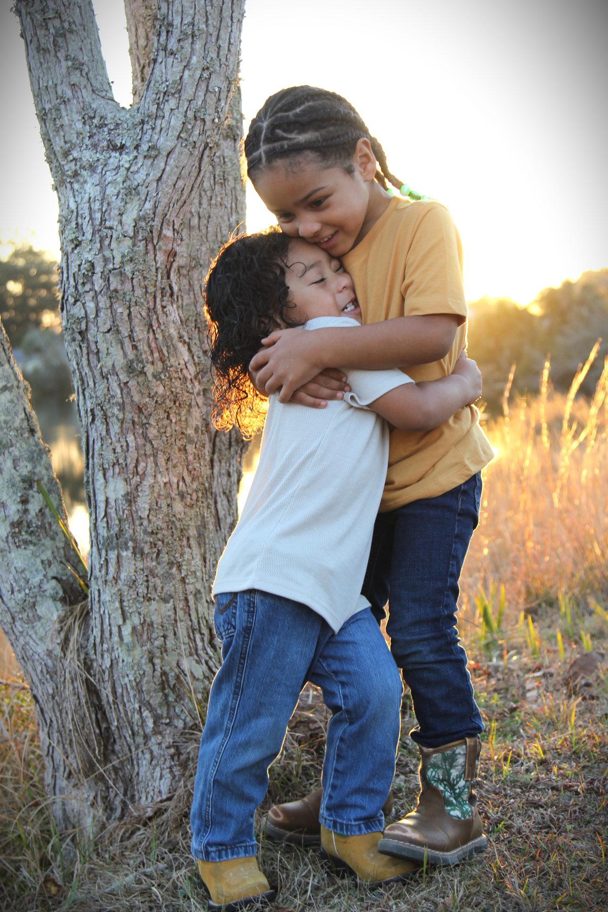 Two children hugging beside an oak tree in a golden field