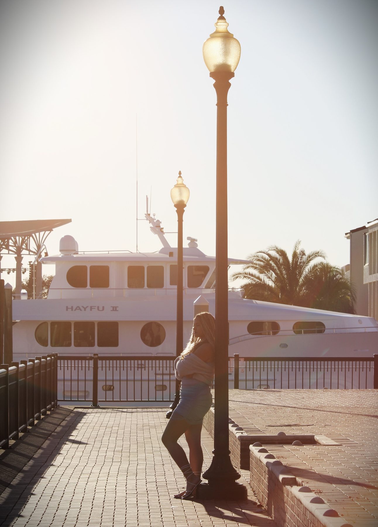 Evening portrait beside a marina lamppost with a yacht in the background