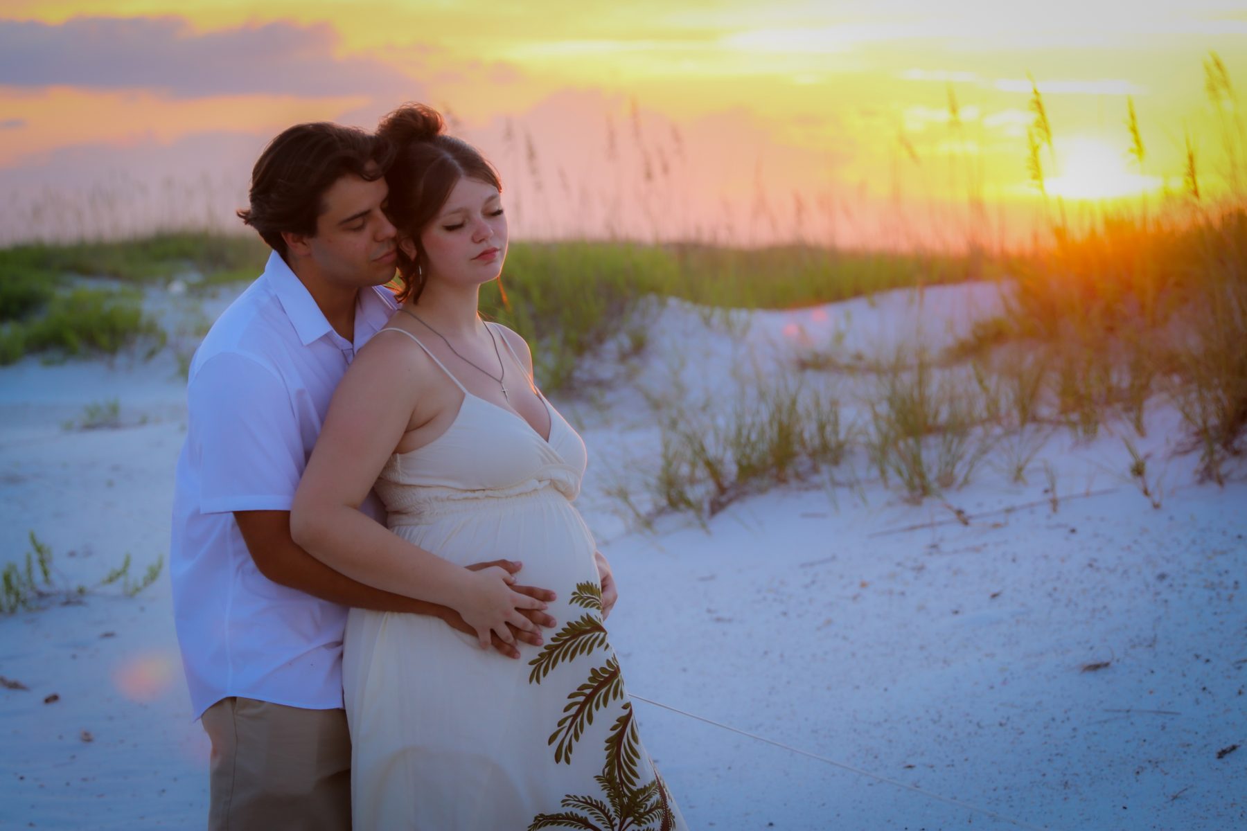 Expecting couple embracing in the sea oats at sunset on Pensacola Beach