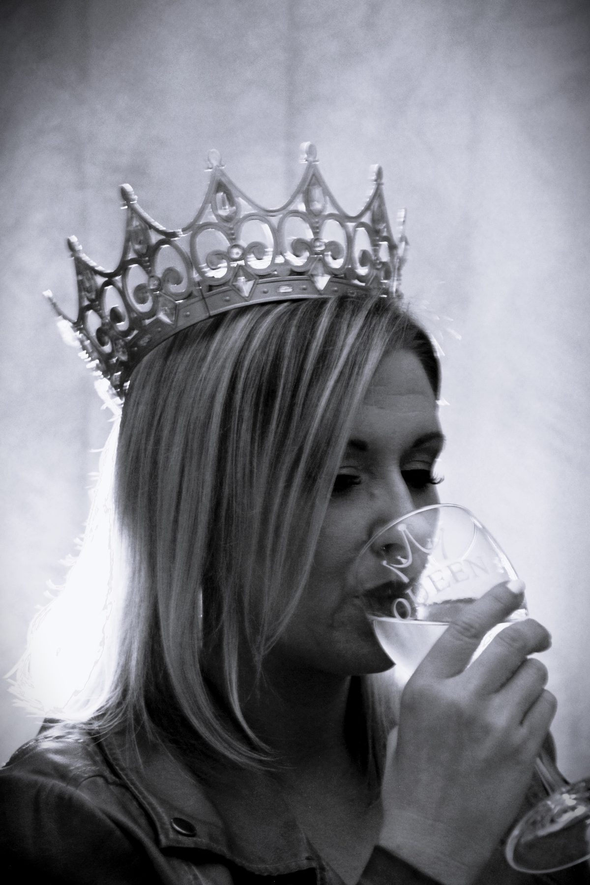 Black-and-white portrait of a woman in a pageant crown raising a glass