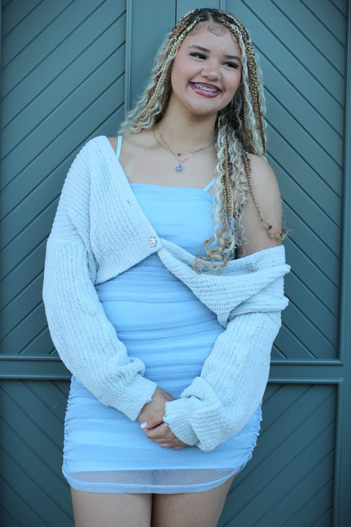 Senior portrait of a smiling young woman in blue against a teal door