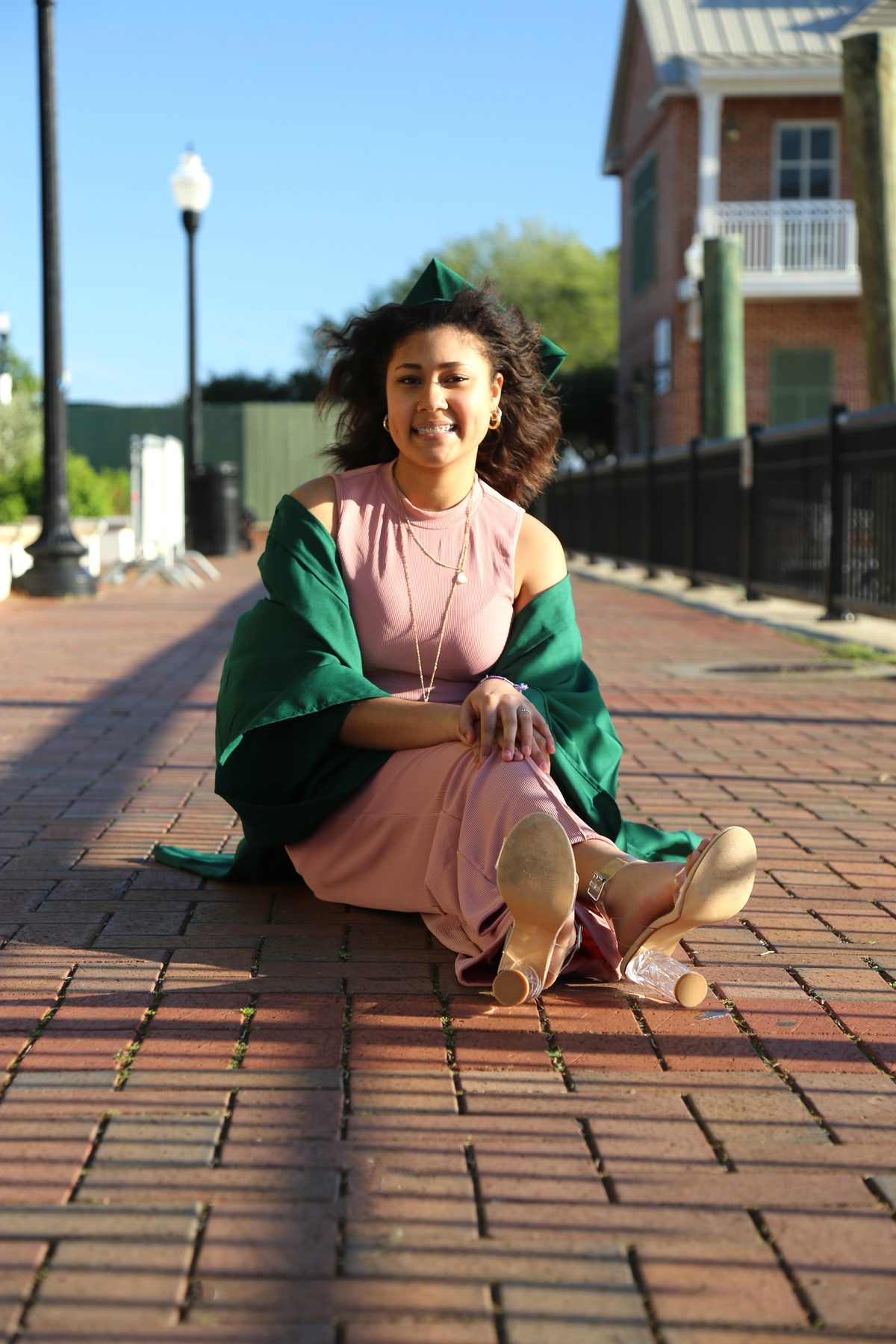 Portrait of a woman in a pink dress and green shawl seated on a brick street in historic downtown Pensacola