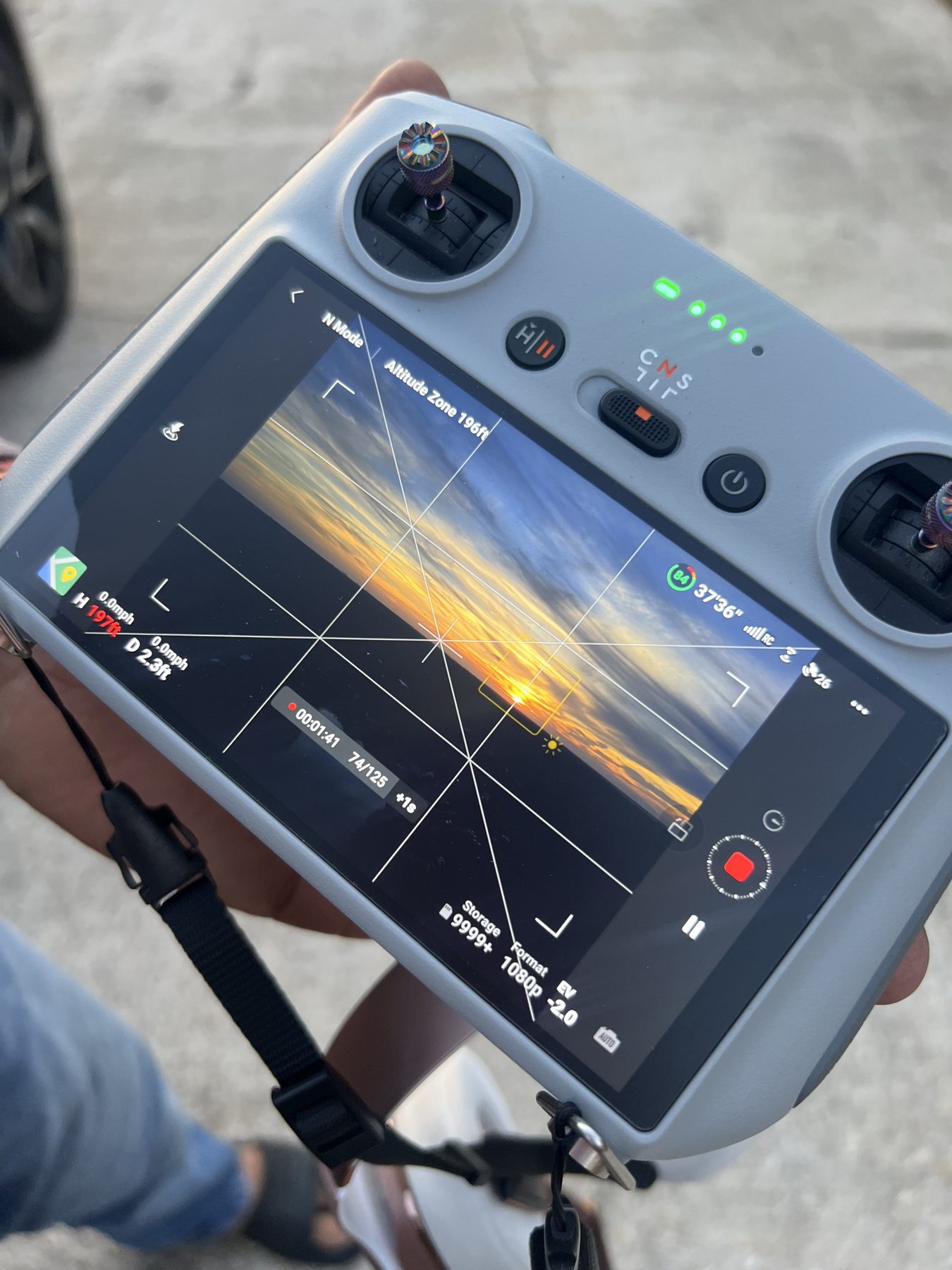 Operator's hands on a drone controller monitoring a sunset aerial shoot