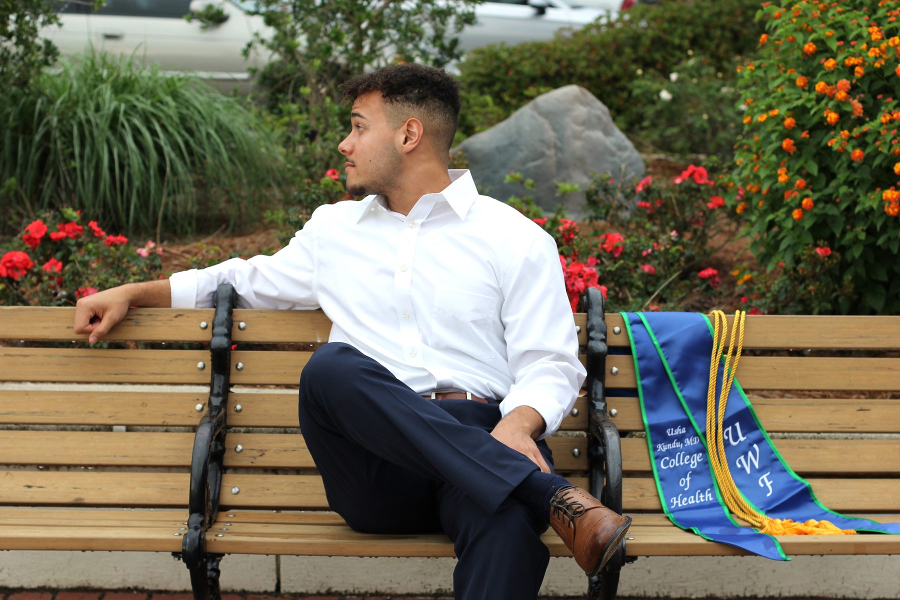 Graduate seated on a park bench beside his commencement stole