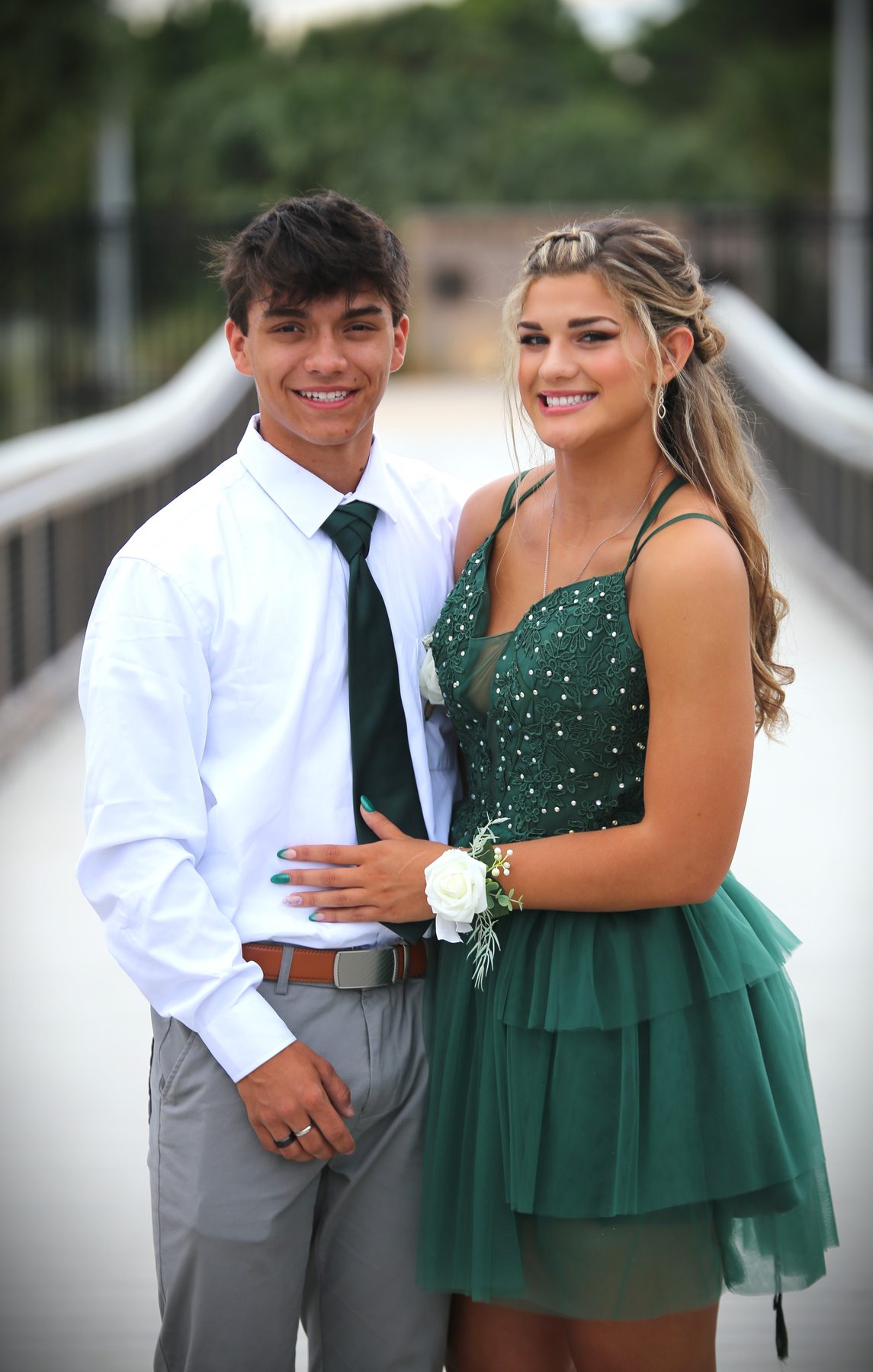 Prom couple in emerald and white posing on a footbridge