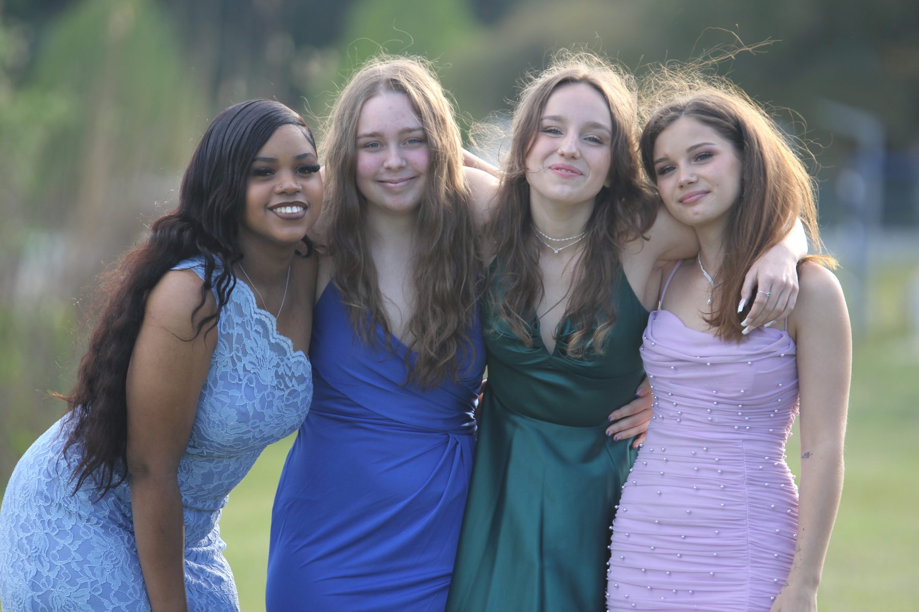 Prom friends in blue, green, and lavender gowns arm in arm