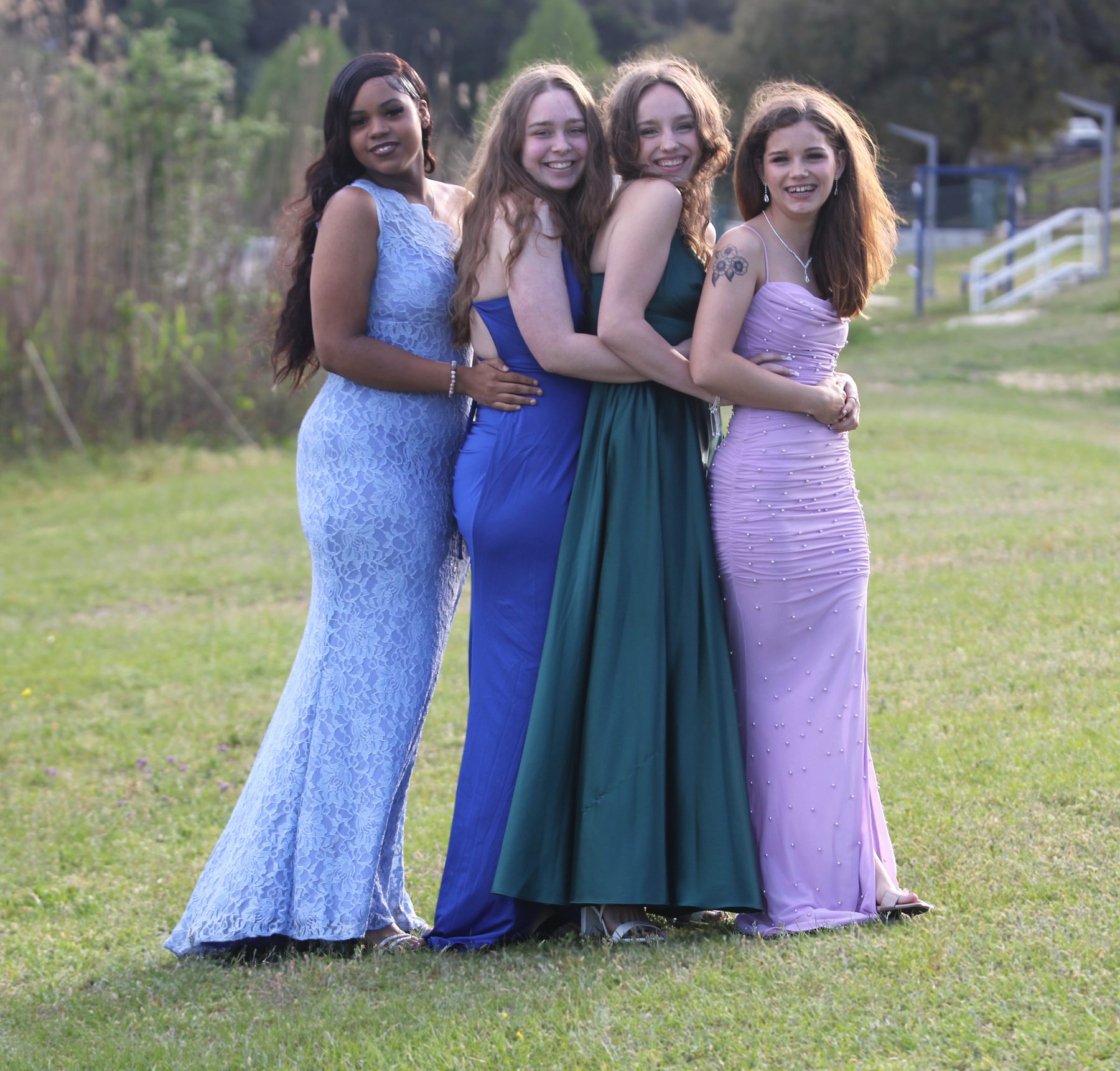 Four friends in prom gowns posing on a green hillside