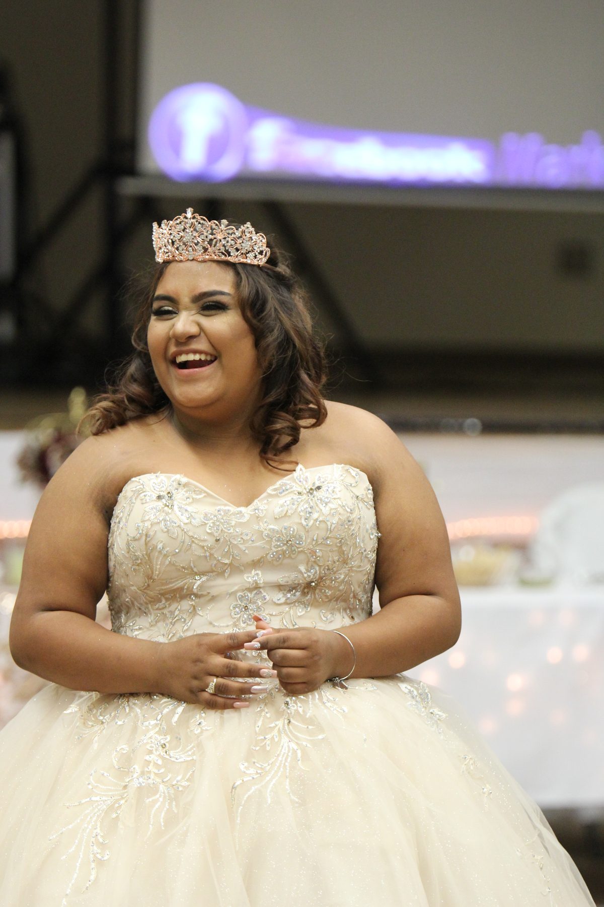 Quinceañera in a tiara and white ball gown smiling at her reception