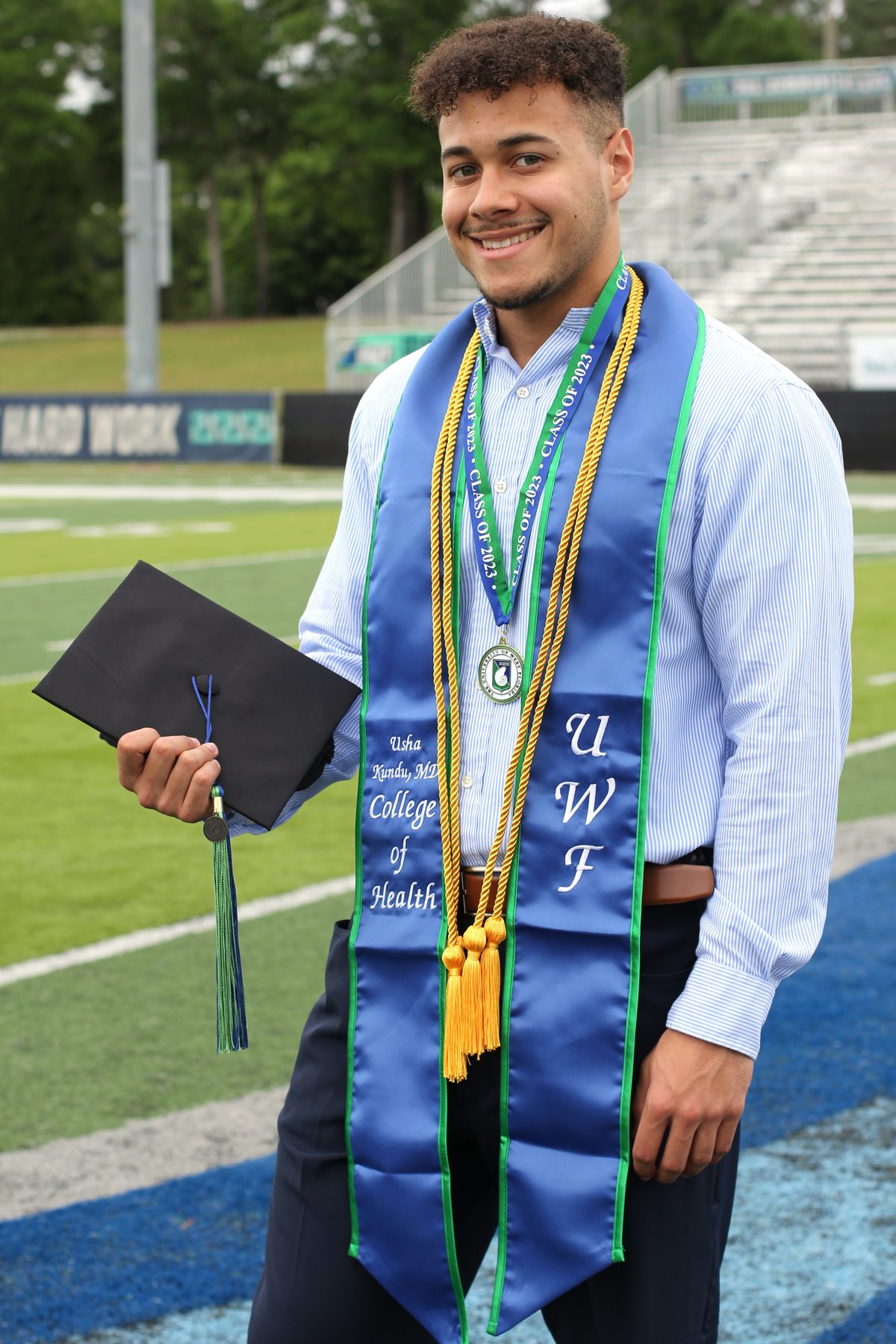 University of West Florida graduate with honor cords on the football field