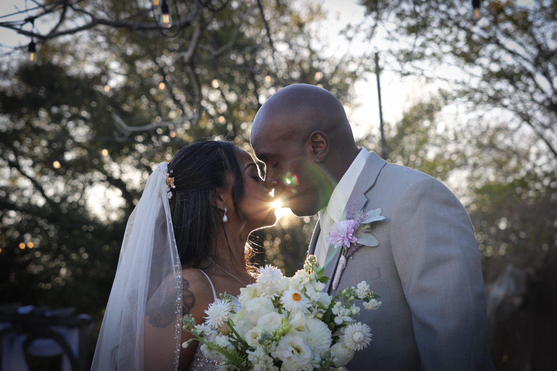 Bride and groom sharing a kiss beneath a live oak tree, white bouquet in hand