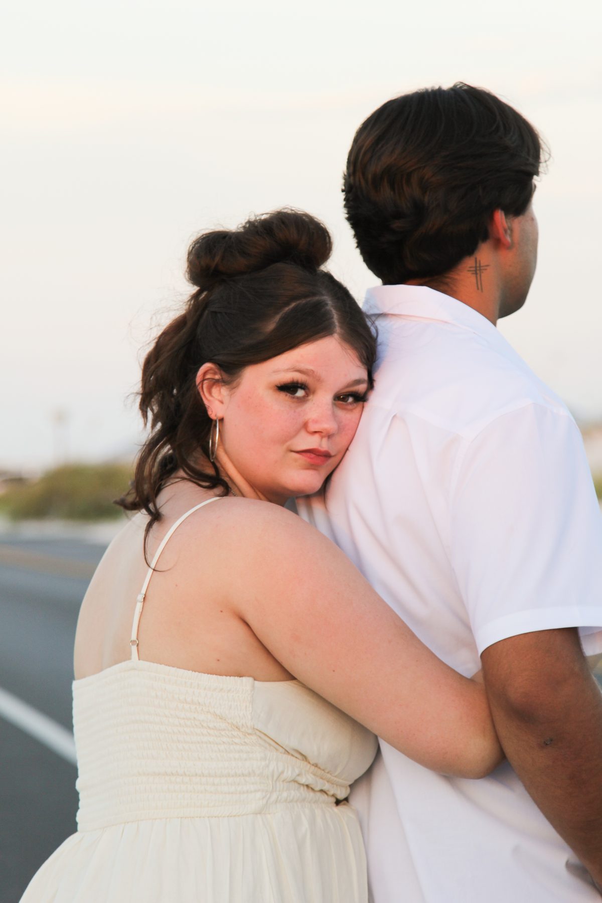Bride-to-be in white embracing her partner along a quiet road at dusk
